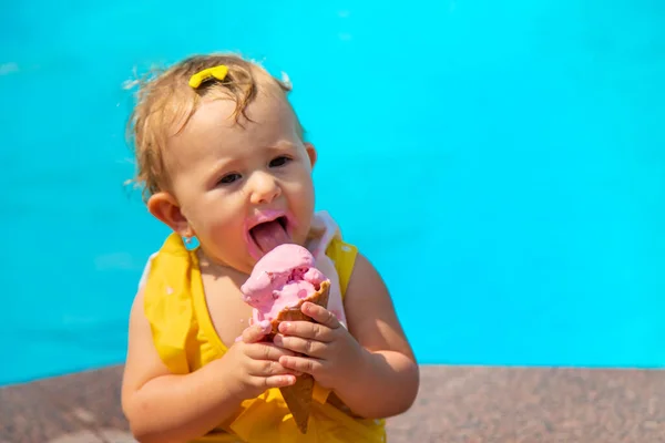 The child is eating ice cream near the pool. Selective focus. Kid.