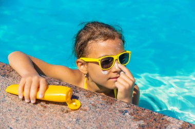 Çocuğun yüzünde havuzun yanında güneş kremi var. Seçici odaklanma. Çocuk.