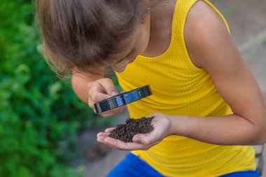 Çocuk bir büyüteçle zemini inceler. Seçici odaklanma. Doğa.