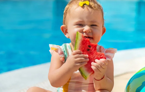 Baby is eating a watermelon by the pool. Selective focus. Kids.