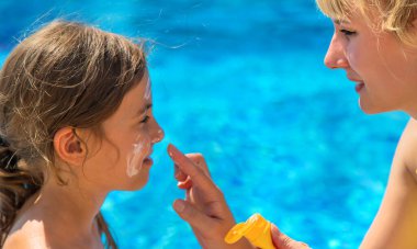 Anne çocuğun yüzüne güneş kremi sürüyor. Seçici odaklanma. Çocuk.