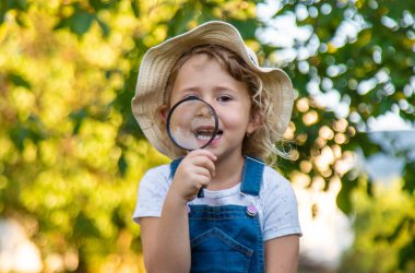 Bir çocuk doğadaki büyüteçten bakar. Seçici odaklanma. Çocuk,