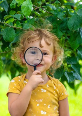 Bir çocuk doğayı büyüteçle inceliyor. Seçici odaklanma. Doğa.