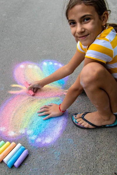 Bir çocuk asfalta tebeşirle bir kelebek çizer. Seçici odaklanma. Çocuk.