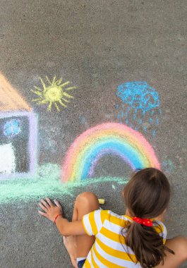 Bir çocuk asfalta tebeşirle bir ev ve gökkuşağı çiziyor. Seçici odaklanma. Çocuk.