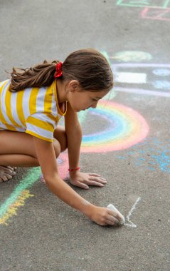 Bir çocuk asfalta tebeşirle bir ev ve gökkuşağı çiziyor. Seçici odaklanma. Çocuk.