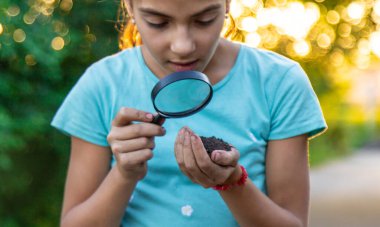 Çocuk bir büyüteçle ellerindeki toprağa bakıyor. Seçici odaklanma. Çocuk,