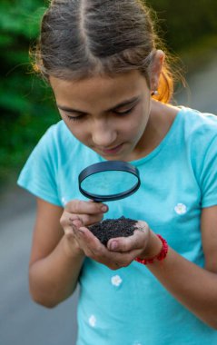 Çocuk bir büyüteçle ellerindeki toprağa bakıyor. Seçici odaklanma. Çocuk,