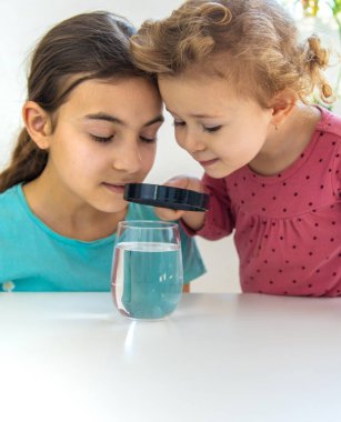 Çocuk bir büyüteç altında suyu inceler. Seçici odaklanma. Çocuk.