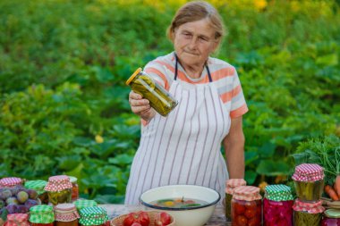 Senior woman preserving vegetables in jars. Selective focus. Food.
