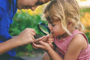 Bir çocuk büyüteçle toprağa bakar. Seçici odaklanma. Çocuk.