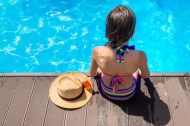 Havuzun yanındaki çocuk güneş kremi sürüyor. Seçime odaklan. Çocuk.