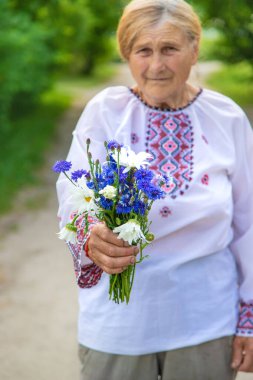 Bir buket çiçekle işlenmiş gömlekli yaşlı bir Ukraynalı kadın. Seçici odaklanma. Doğa.