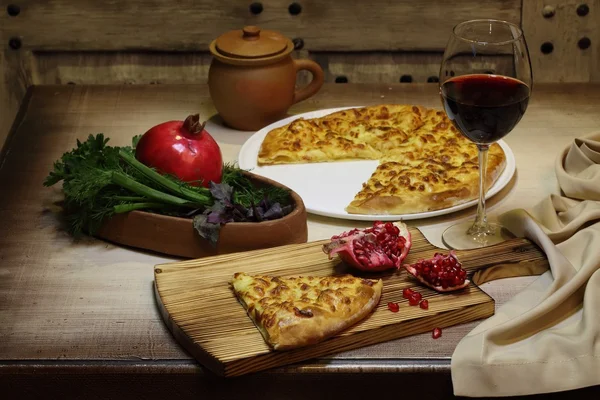 Vin rouge dans un verre et grenade gâteau au fromage sur table en bois — Photo