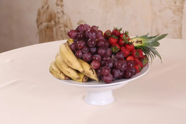 Jordgubbar, bananer, ananas och druvor - frukter på en tallrik — Stockfoto