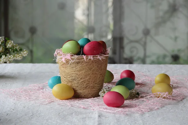 Huevos de Pascua en cesta y sobre la mesa — Foto de Stock
