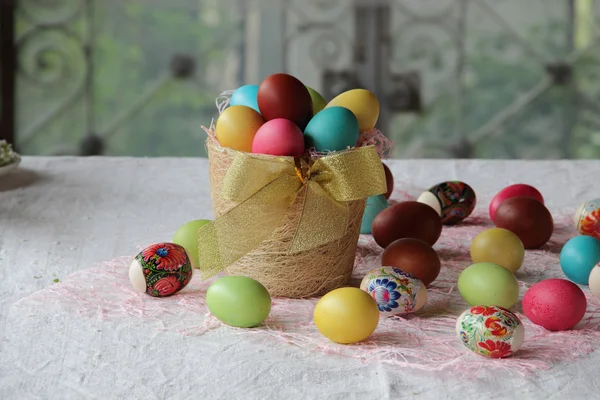 Huevos de Pascua en cesta y sobre la mesa — Foto de Stock