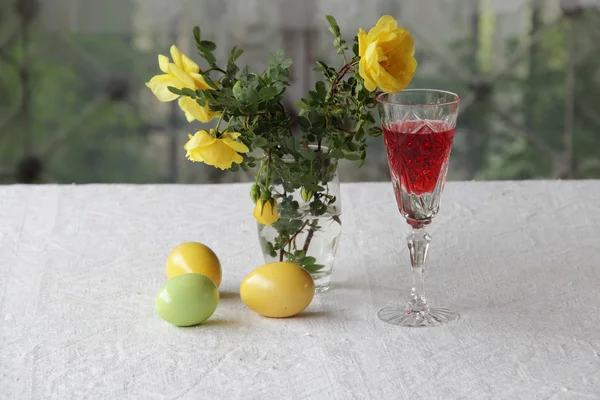 Красное вино в стакане и пасхальные яйца и букет роз — стоковое фото