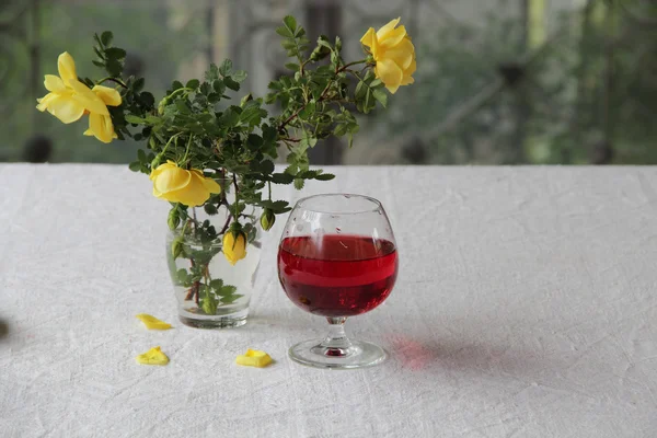 Vino tinto en la copa y un ramo de rosas amarillas — Foto de Stock