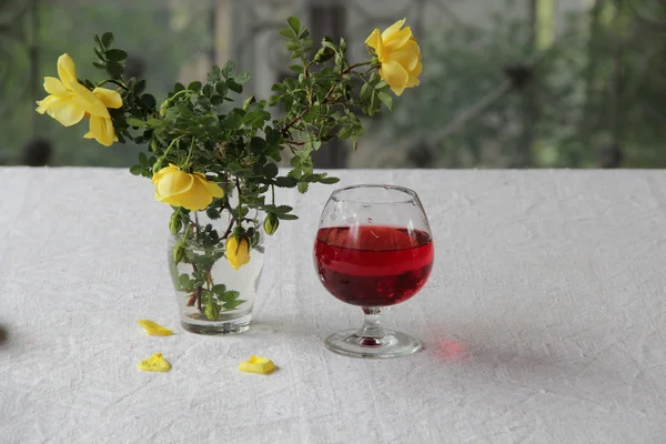 Vinho tinto em um copo transparente e um buquê de rosas — Fotografia de Stock