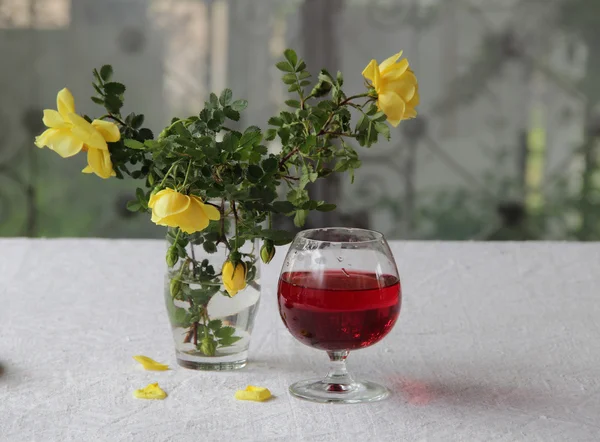 Κόκκινο κρασί σε ένα διαφανές γυαλί και ένα μπουκέτο από τριαντάφυλλα — Φωτογραφία Αρχείου