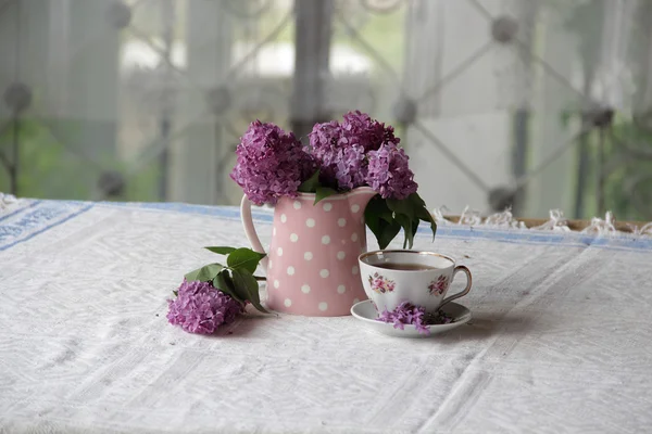 Uma xícara de chá e um buquê de lilases na mesa — Fotografia de Stock