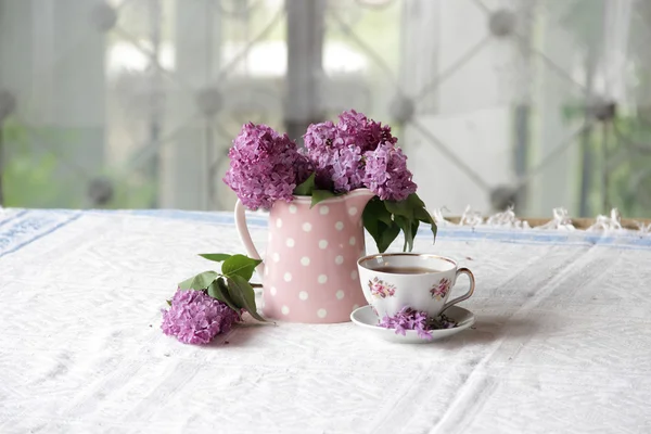 Uma xícara de chá e um buquê de lilases na mesa — Fotografia de Stock