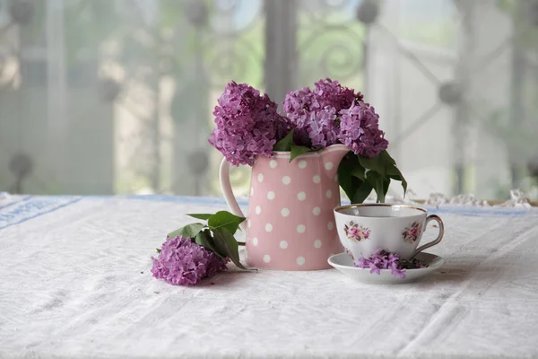 Une tasse de thé et un bouquet de lilas sur la table — Photo