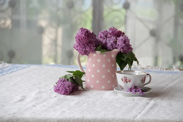 Uma xícara de chá e um buquê de lilases na mesa — Fotografia de Stock