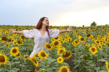 Çiçek açan ayçiçeklerinin arasında beyaz elbiseli bir kız