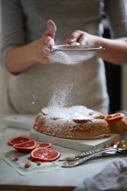 Pudra şekeri elekten portakallı turtaya dökülür.