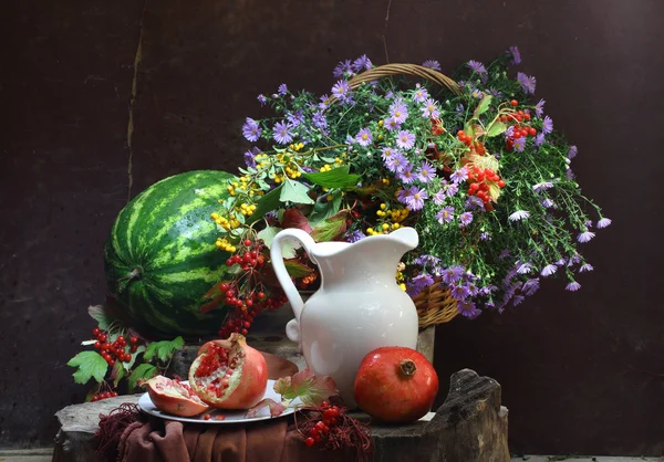 Water-meloen, een granaatappel, een witte kruik en een boeket in een wattl — Stockfoto