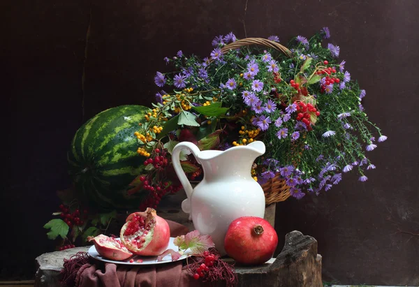 Water-meloen, een granaatappel, een witte kruik en een boeket in een wattl — Stockfoto