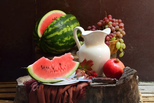 Trauben, ein Granatapfel, eine Wassermelone und ein weißer Krug — Stockfoto