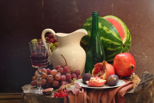 Vin, druvor, ett granatäpple, en figur, en vattenmelon och en vit ju — Stockfoto