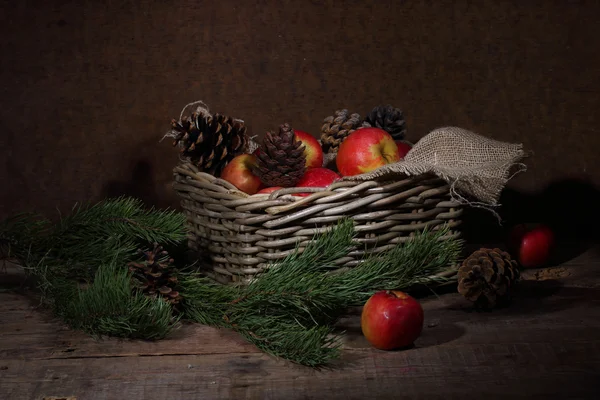 Manzanas y conos en una cesta de mimbre y una rama de pino — Foto de Stock