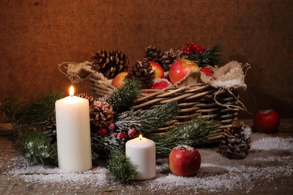 Manzanas y conos en una cesta de mimbre, velas y una rama de pino , — Foto de Stock