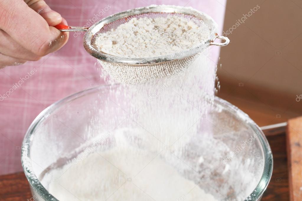 The man's hand sifts a flour in a cup through a sieve