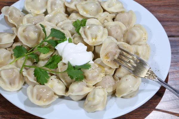 Pelmeni mit saurer Sahne, Butter, einem Zweig Petersilie und Boden — Stockfoto