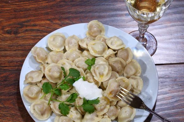 Ekşi krema ve şeffaf bir bardak beyaz şarap ile mantı