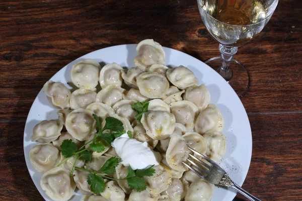 Ekşi krema ve şeffaf bir bardak beyaz şarap ile mantı