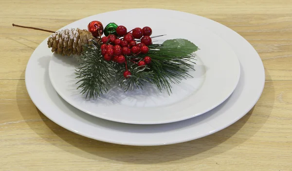 Ramo di un pino artificiale con bacche rosse e piatti bianchi — Foto Stock