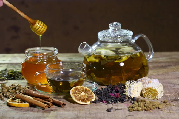 Honey flows in bank near to a teapot and a cup of tea — Stock Photo, Image