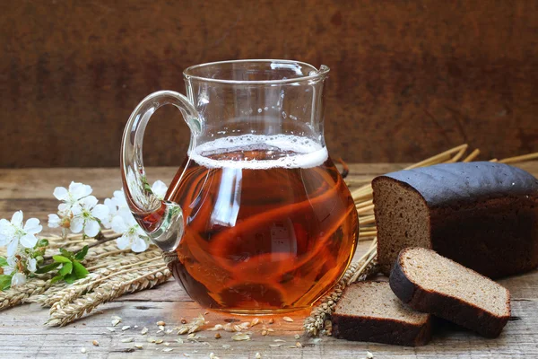 Karaf met kvas en roggebrood op een houten tafel — Stockfoto