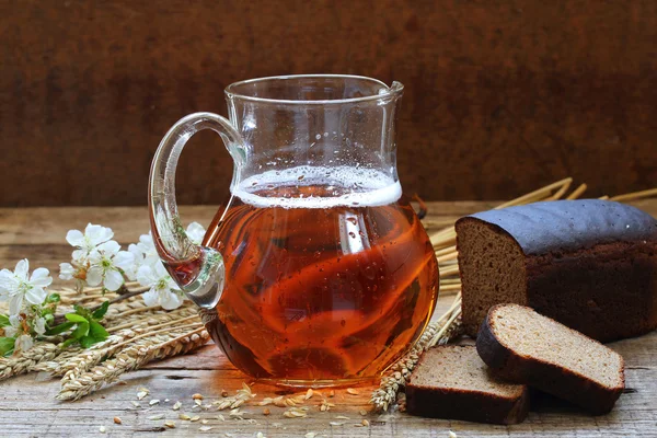 Karaf met kvas en roggebrood op een houten tafel, kegels en een blos — Stockfoto