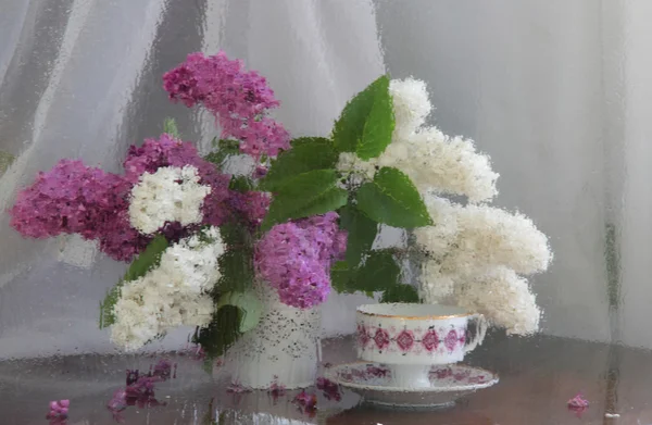 Still-life with a lilac and a cup of tea behind wet glass — Stock Photo, Image