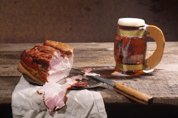 Beer with foam in a transparent mug and smoked meat with a fat l — Stock Photo, Image