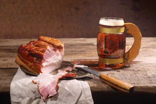 Beer with foam in a transparent mug and smoked meat with a fat l — Stock Photo, Image
