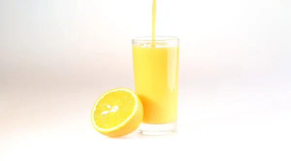 Orange juice a stream flows in a transparent glass, a glass with — Zdjęcie stockowe