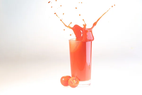 Splash em suco de tomate em um vidro transparente em um backgro branco — Fotografia de Stock